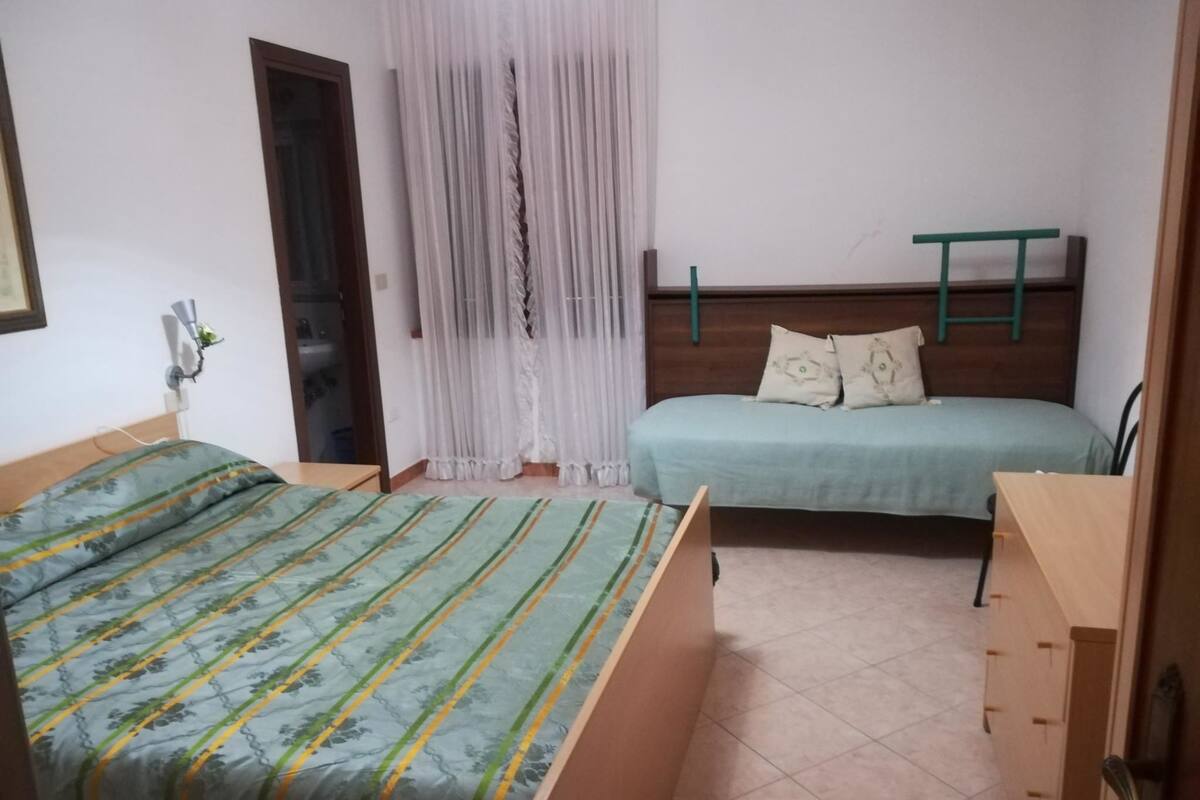 A bedroom with two beds, a wooden headboard, a small desk, and a window with sheer curtains.