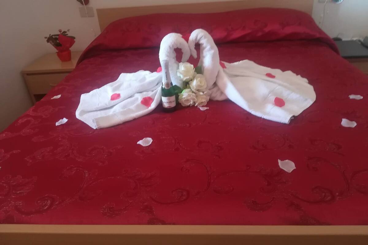 A bed with a red bedspread and a bouquet of white roses placed on it.