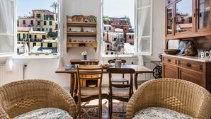 Una habitación acogedora con muebles de mimbre, una mesa de madera y vistas a edificios coloridos a través de ventanas abiertas.