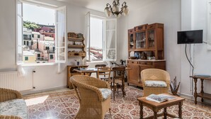 Una sala de estar acogedora con un ventanal grande, muebles de mimbre, un candelabro y un televisor montado en la pared.