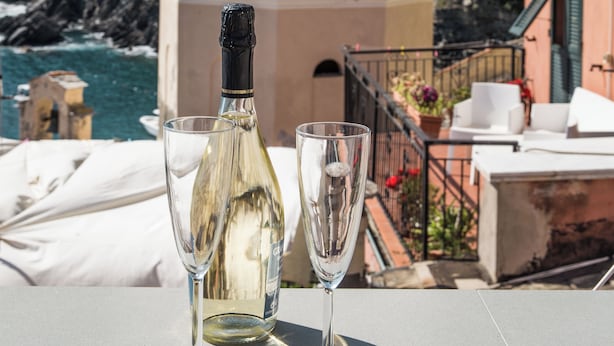 Una mesa con una botella de vino blanco y dos copas, frente a un edificio costero con cúpula y balcón con vistas al mar.