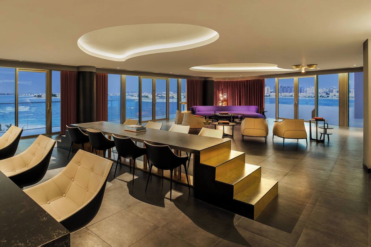 Een moderne woonkamer met een grote eettafel, comfortabele zitplaatsen en een stadszicht door grote ramen.