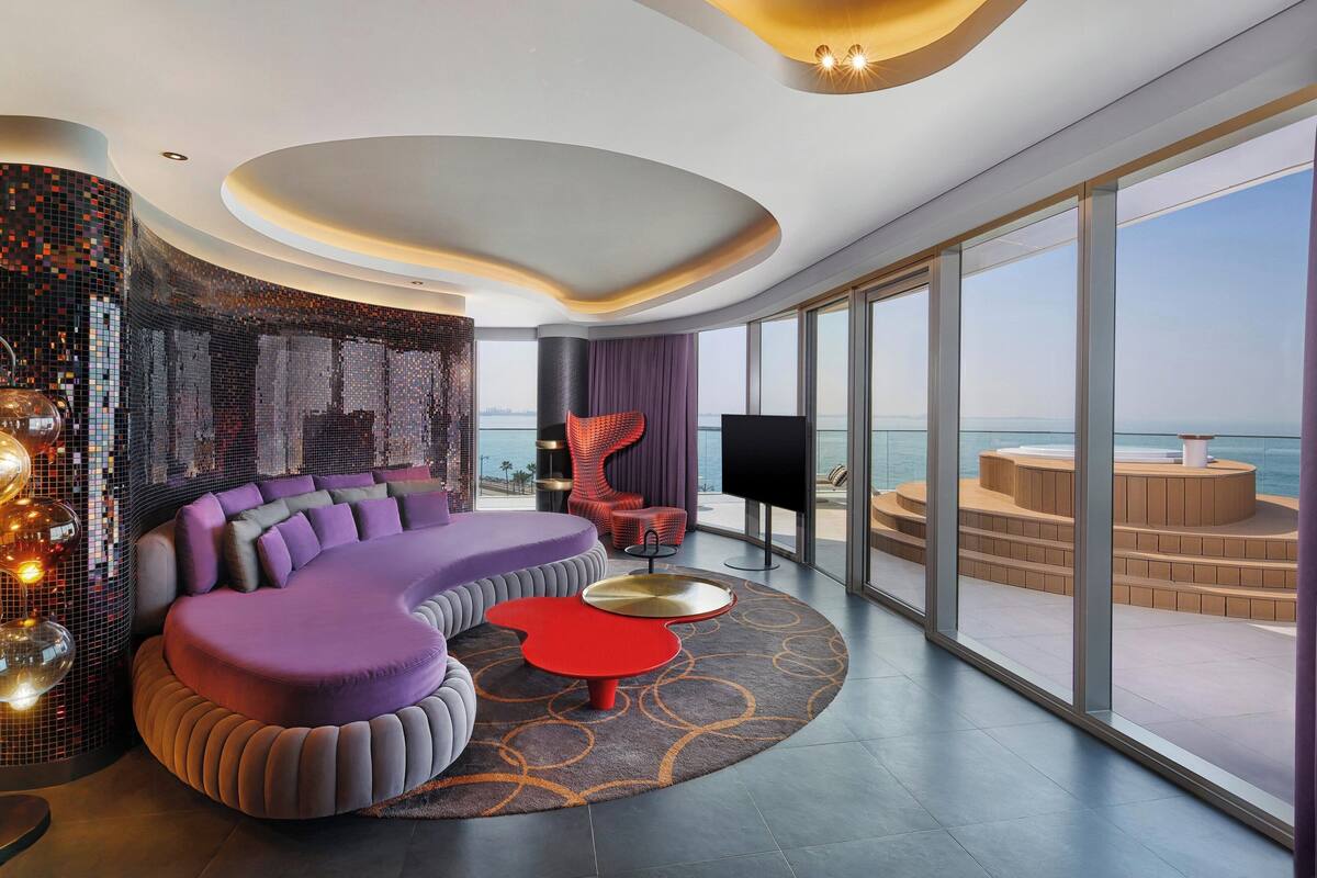 Een moderne woonkamer met een gebogen bank, een rode salontafel en een groot raam met uitzicht op zee.