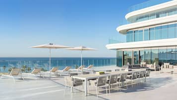 A rooftop terrace with sun loungers, a dining area, and a view of the ocean.