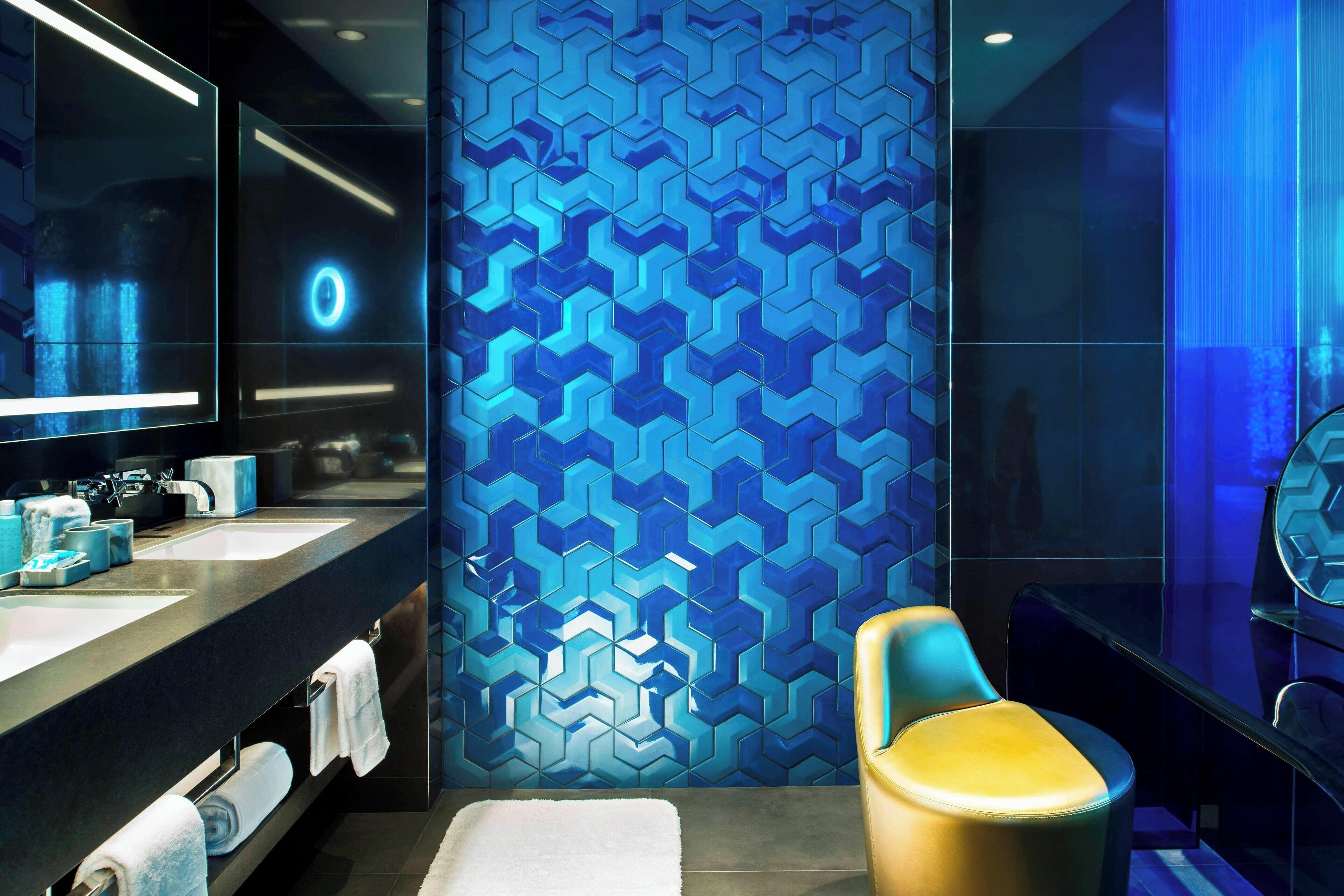 Une salle de bain moderne avec un grand miroir, deux vasques, un porte-serviettes et un mur orné d’un motif géométrique.