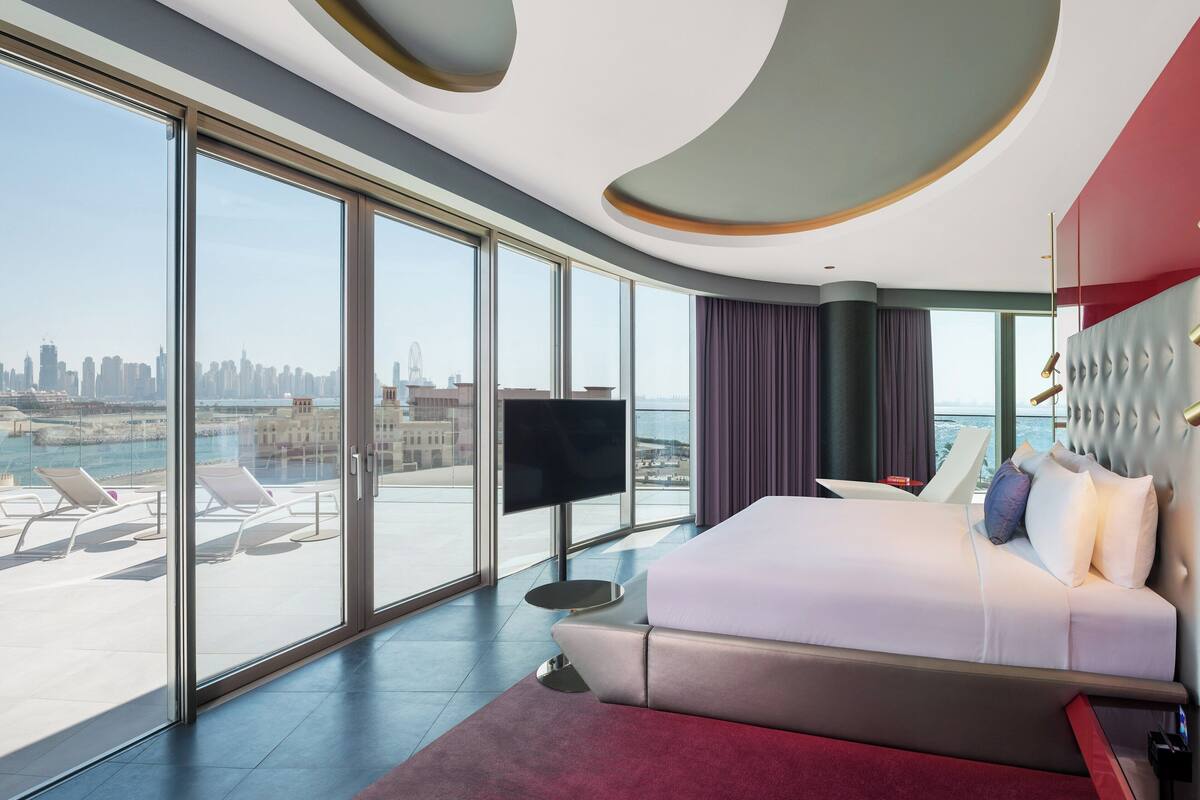 Een moderne hotelkamer met een groot bed, een televisie en uitzicht op een stadshemelbeeld en water.