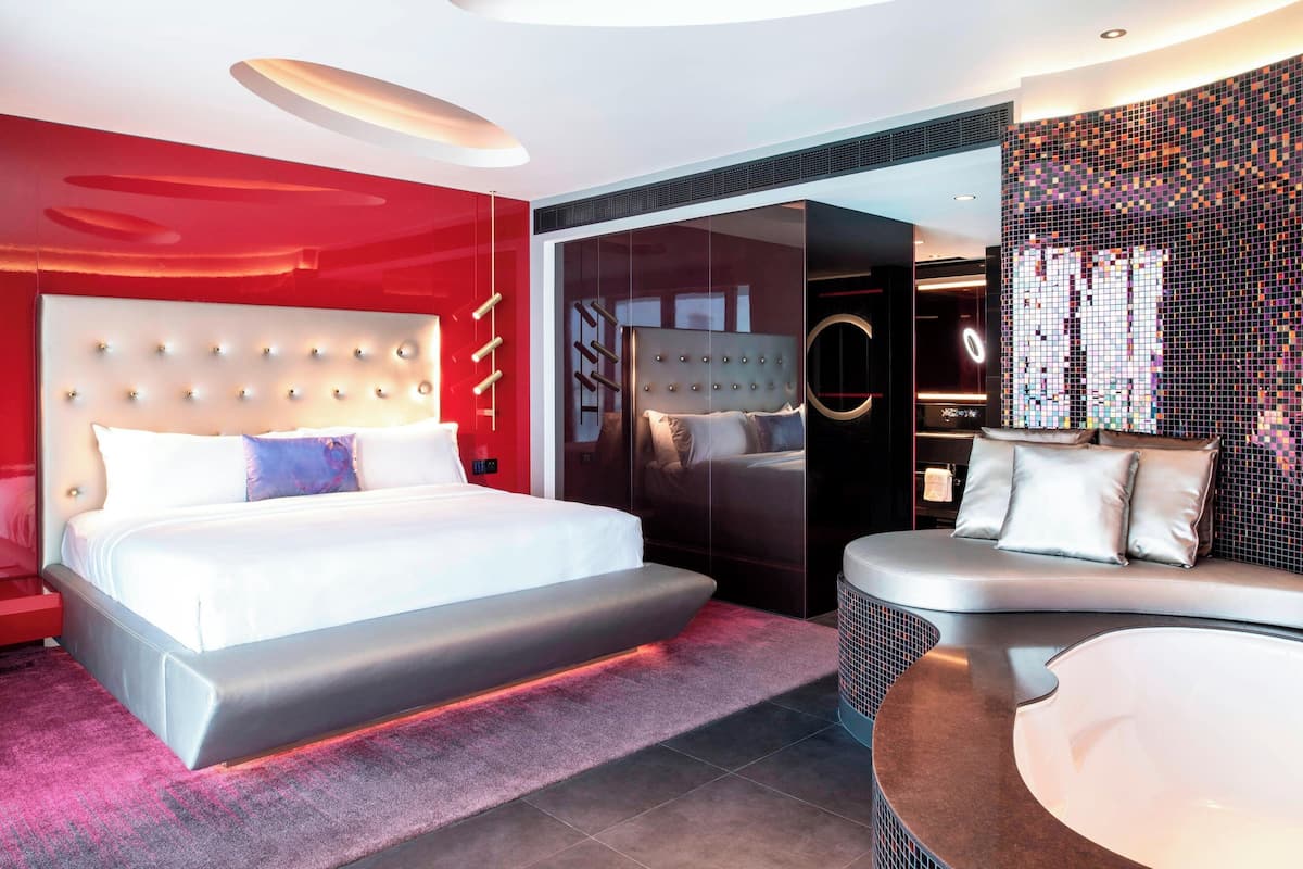 Een moderne slaapkamer met een groot bed, een zithoek met een gebogen bank en een glazen scheiding.