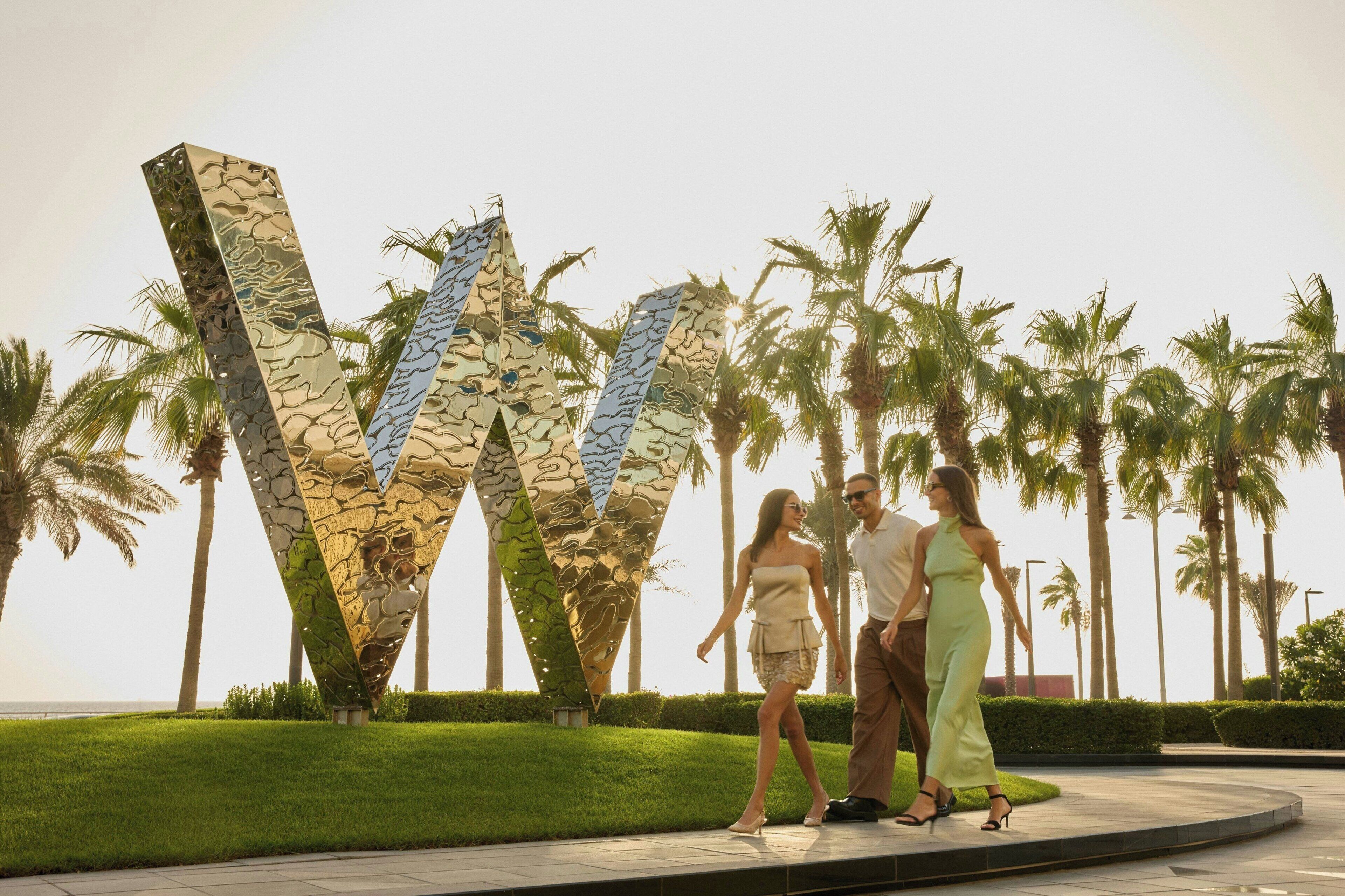 A modern sculpture with geometric shapes and a reflective surface, surrounded by palm trees and a well-maintained lawn.