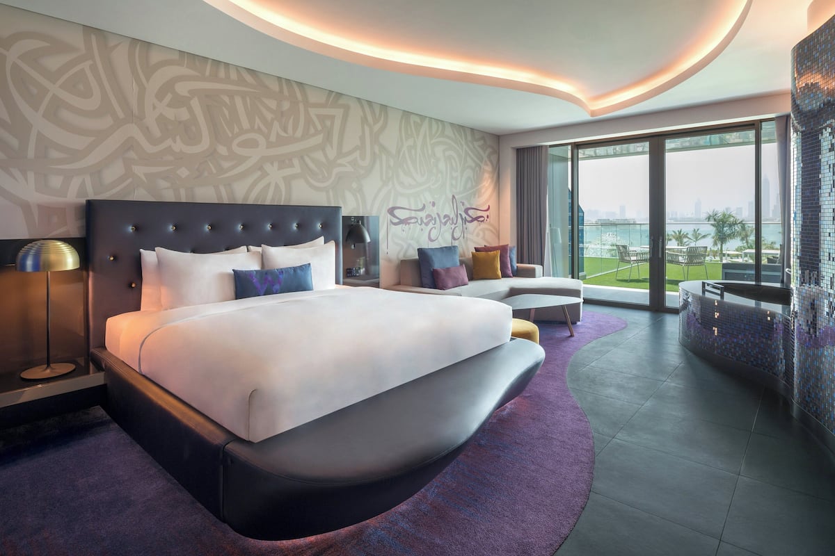 Een moderne hotelkamer met een groot bed, een bank, een balkon met uitzicht op de stad en een decoratieve muur met kalligrafie.