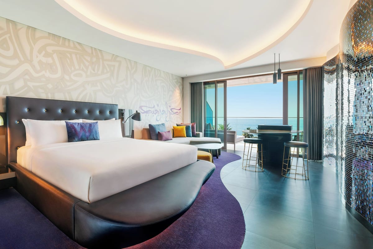 Een moderne hotelkamer met een groot bed, een zithoek, een bar en uitzicht op zee.