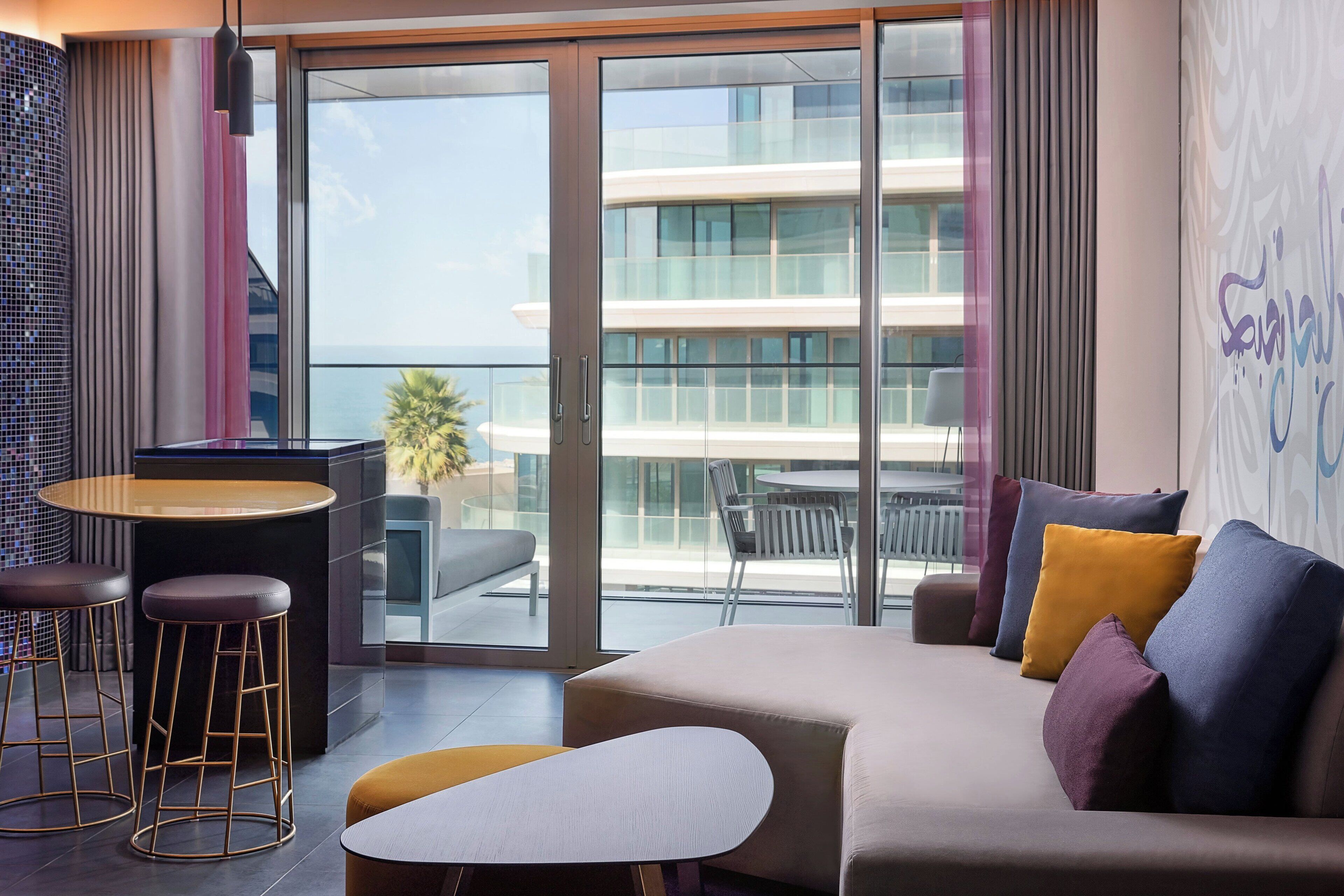 Une chambre d’hôtel moderne dotée d’un canapé, d’un petit coin bar et d’un balcon offrant une vue sur la ville.