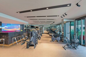 A modern gym with various exercise equipment, a reception area, and large windows offering views.