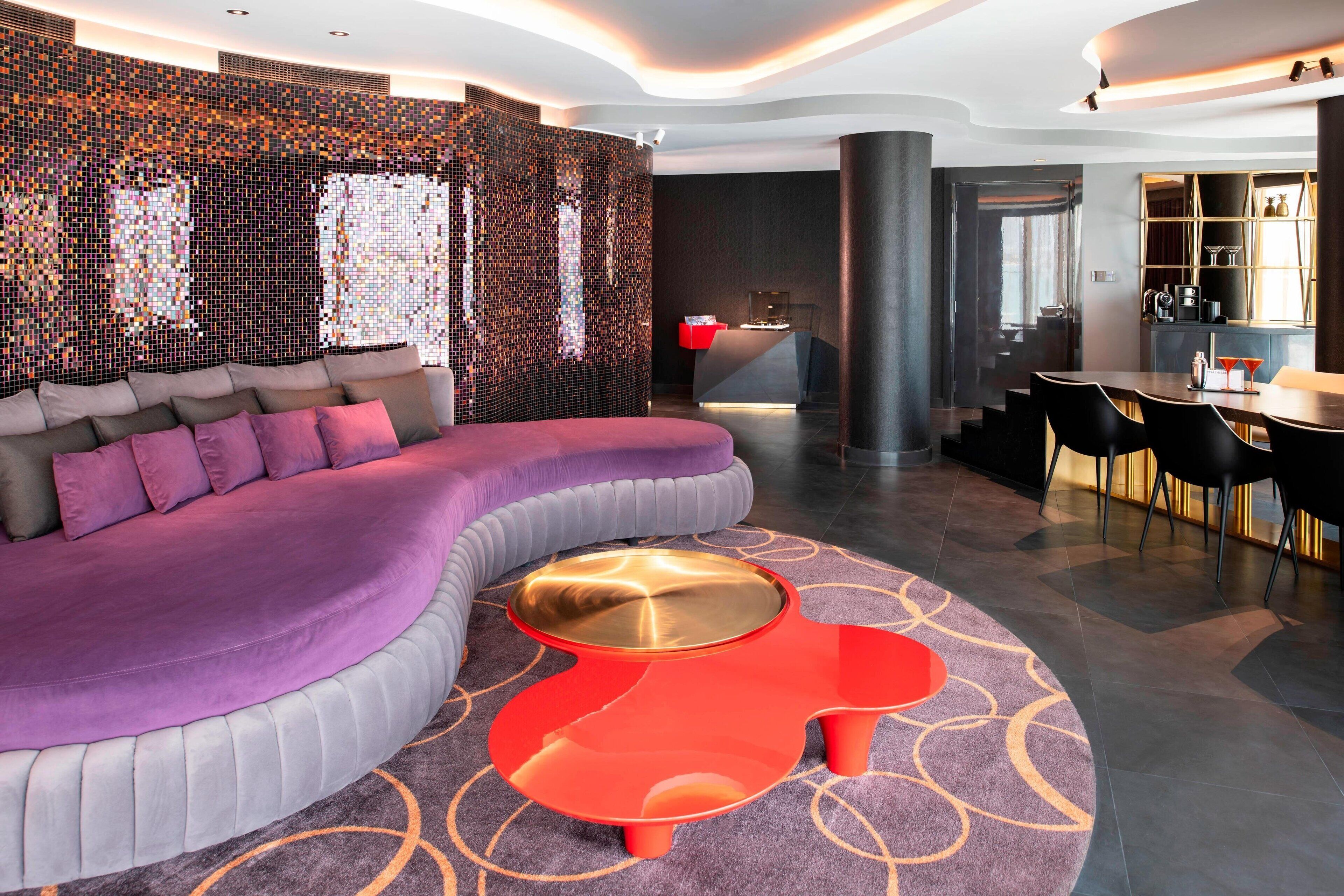 A modern hotel lobby with a curved purple sofa, a red coffee table, and a patterned carpet.