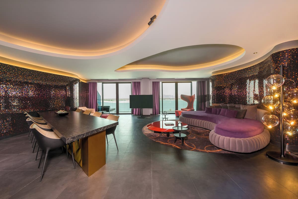 Een moderne hotelkamer met een gebogen plafond, een grote eettafel, een bank en een televisie.