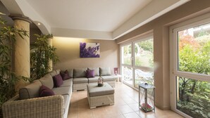 Un salon moderne avec un canapé d’angle, une petite table et une grande fenêtre donnant sur l’extérieur.