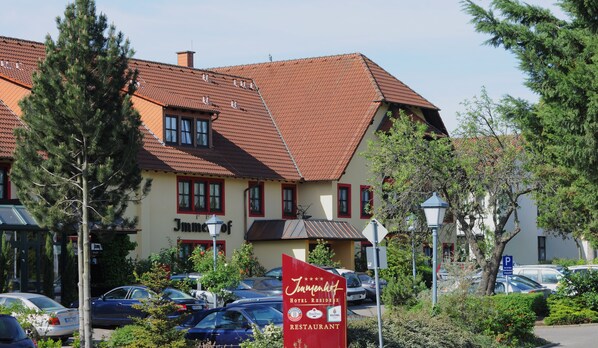 Ein Hotel mit rotem Ziegeldach, zahlreichen Fenstern und einem Schild, das einen Restaurantbetrieb und Hotelzimmer anzeigt.