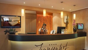 Un comptoir d’accueil d’hôtel au design moderne, avec un téléviseur fixé au-dessus et un grand miroir qui reflète la pièce.