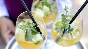 A tray with two glasses of a yellow beverage, each garnished with mint leaves and a black straw.