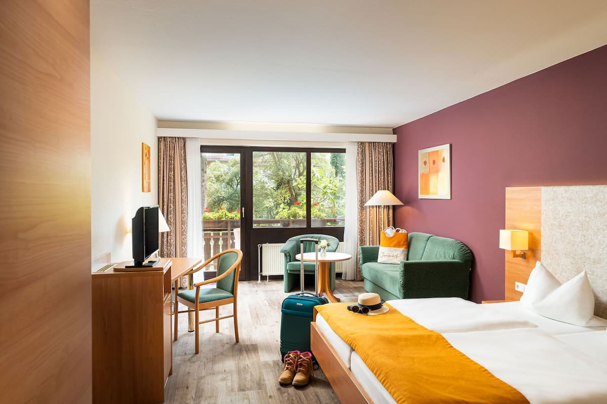 Ein Hotelzimmer mit Bett, Schreibtisch, Stuhl, Tisch und Blick auf Grünflächen.
