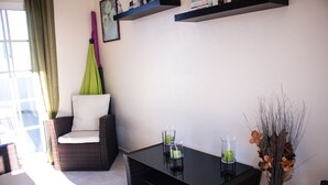 A modern living room with a dark wicker sofa, a glass coffee table, and a vase with dried flowers.