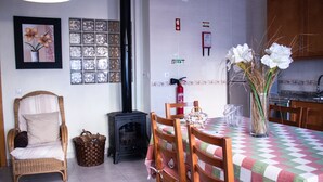 A dining area with a checkered tablecloth, wicker chairs, a wicker sofa, a fireplace, and a vase with flowers.