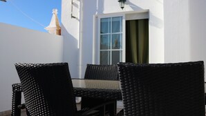 A white building with a window and a door, a table, and two chairs.