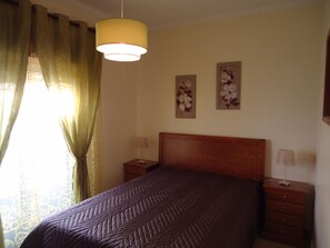 A bedroom with a bed, two bedside tables, a hanging lamp, and two wall-mounted flower paintings. - Casa Antonio C (Alvor)