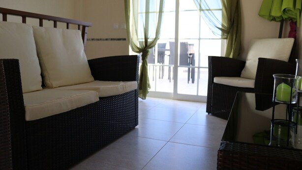 A living room with a sofa and armchairs, a glass coffee table, and a view of the outside.