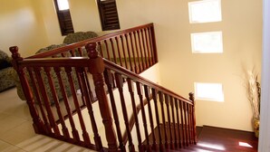 A wooden staircase with a handrail, leading to a landing with a patterned rug. - Villa Cannelles (Micoud)