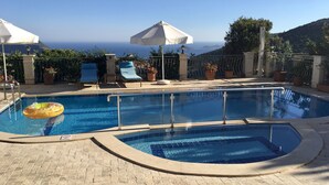Une piscine avec vue sur la mer, entourée de chaises longues et de parasols.