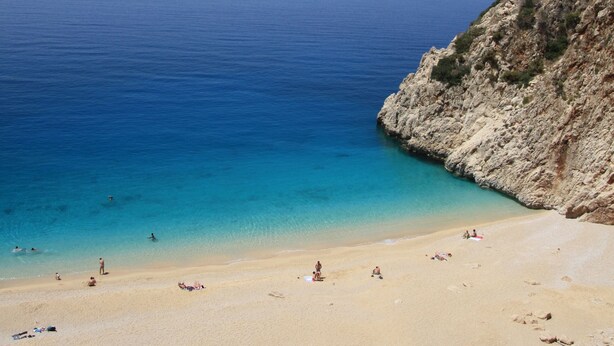 Une plage à l’eau d’un bleu limpide, bordée d’un rivage sablonneux et de falaises rocheuses.