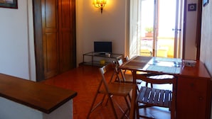 A compact living space with a wooden dining table, chairs, a television, and a wall-mounted lamp. - HOUSE WITH TERRACE AND SEA VIEW (Positano)