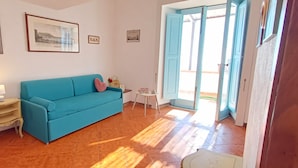 A room with a blue sofa, a small table with a lamp, and a door leading outside. - HOUSE WITH TERRACE AND SEA VIEW (Positano)