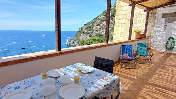 A table set for dining with a view of the sea and a stone building. - HOUSE WITH TERRACE AND SEA VIEW (Positano)