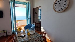 A dining area with a table set for two, a view of the sea through open doors, a wall-mounted clock, and a television on the wall. - HOUSE WITH TERRACE AND SEA VIEW (Positano)