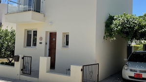 A two-story building with a balcony, a small garden, and a parked car. - Detached Villa In Cul-de-Sac With Private Pool And Sea Views & Free WiFi. (Peyia. Paphos)