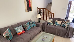 A living room with two grey sofas, colorful cushions, a glass coffee table, a lamp, and a staircase in the background. - Detached Villa In Cul-de-Sac With Private Pool And Sea Views & Free WiFi. (Peyia. Paphos)