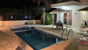 A swimming pool with a tiled deck, a covered patio area with outdoor furniture, and a two-story building with balconies. - Detached Villa In Cul-de-Sac With Private Pool And Sea Views & Free WiFi. (Peyia. Paphos)