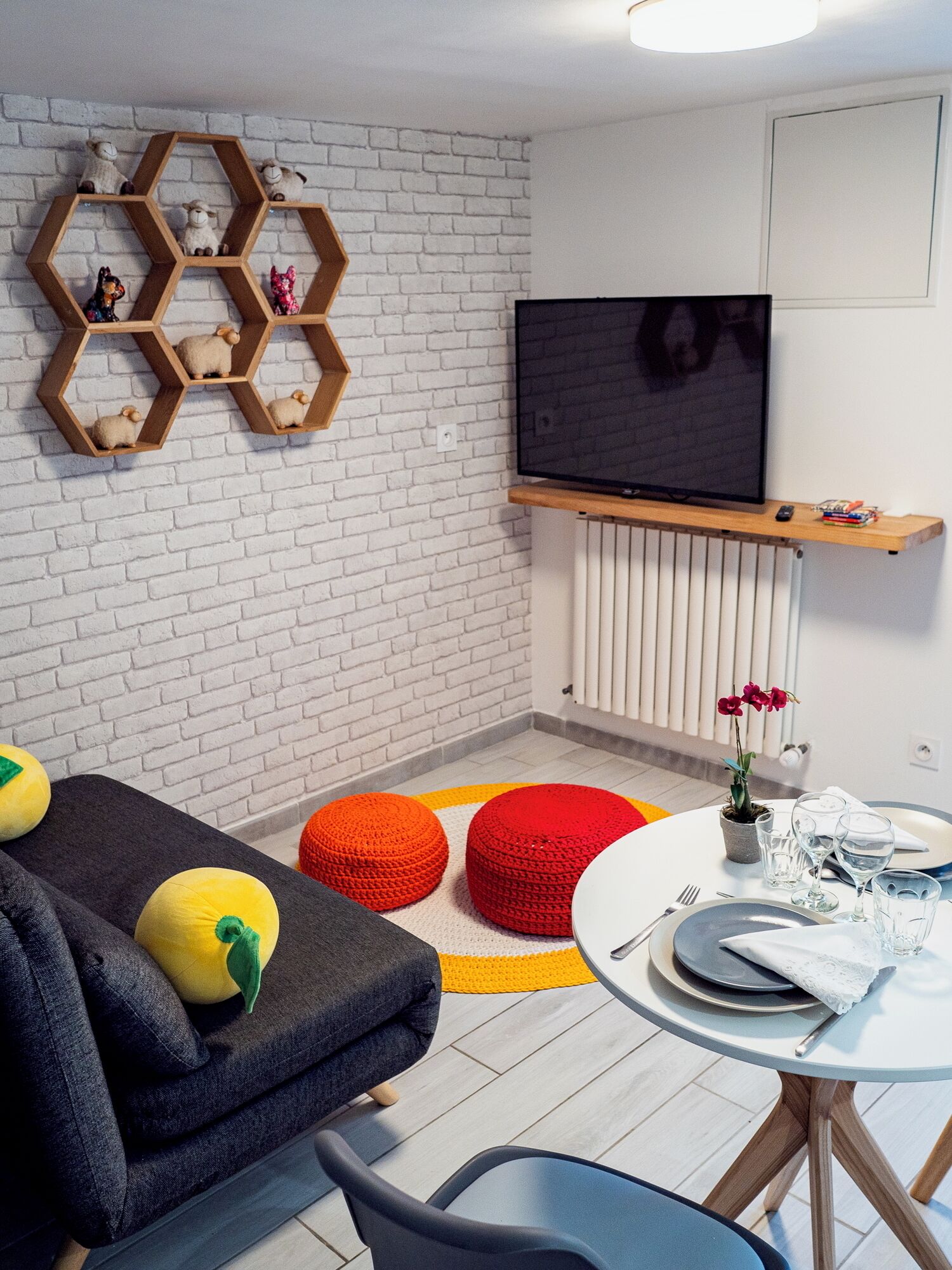 A modern living room with a white brick wall, a mounted TV, and a dining area with a round table and chairs.