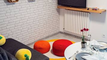 A modern living room with a white brick wall, a mounted TV, and a dining area with a round table and chairs.