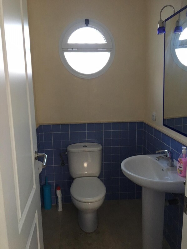 A bathroom with a toilet, sink, and a round window above the toilet. - Luxury villa with private pool overlooking golf course, close to beach (Cartaya (Huelva))