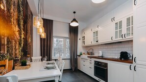 A modern kitchen with white cabinets, a wooden countertop, and a dining area with a white table and chairs. - ShortStayPoland Marszałkowska - B28 (Warsaw)