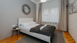A neatly made bed with a white headboard, a bedside table with a lamp, and a window with sheer curtains. - ShortStayPoland Marszałkowska - B28 (Warsaw)