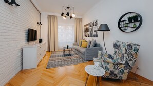 A modern living room with a white brick wall, a grey sofa, a patterned armchair, a round coffee table, a TV on a white cabinet, and a black lamp. - ShortStayPoland Marszałkowska - B28 (Warsaw)