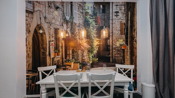 A dining area with a rustic stone wall backdrop, white table and chairs, and hanging light fixtures. - ShortStayPoland Marszałkowska - B28 (Warsaw)