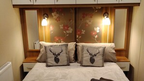 A double bed with a floral headboard, two nightstands, a mirror, and two lamps.