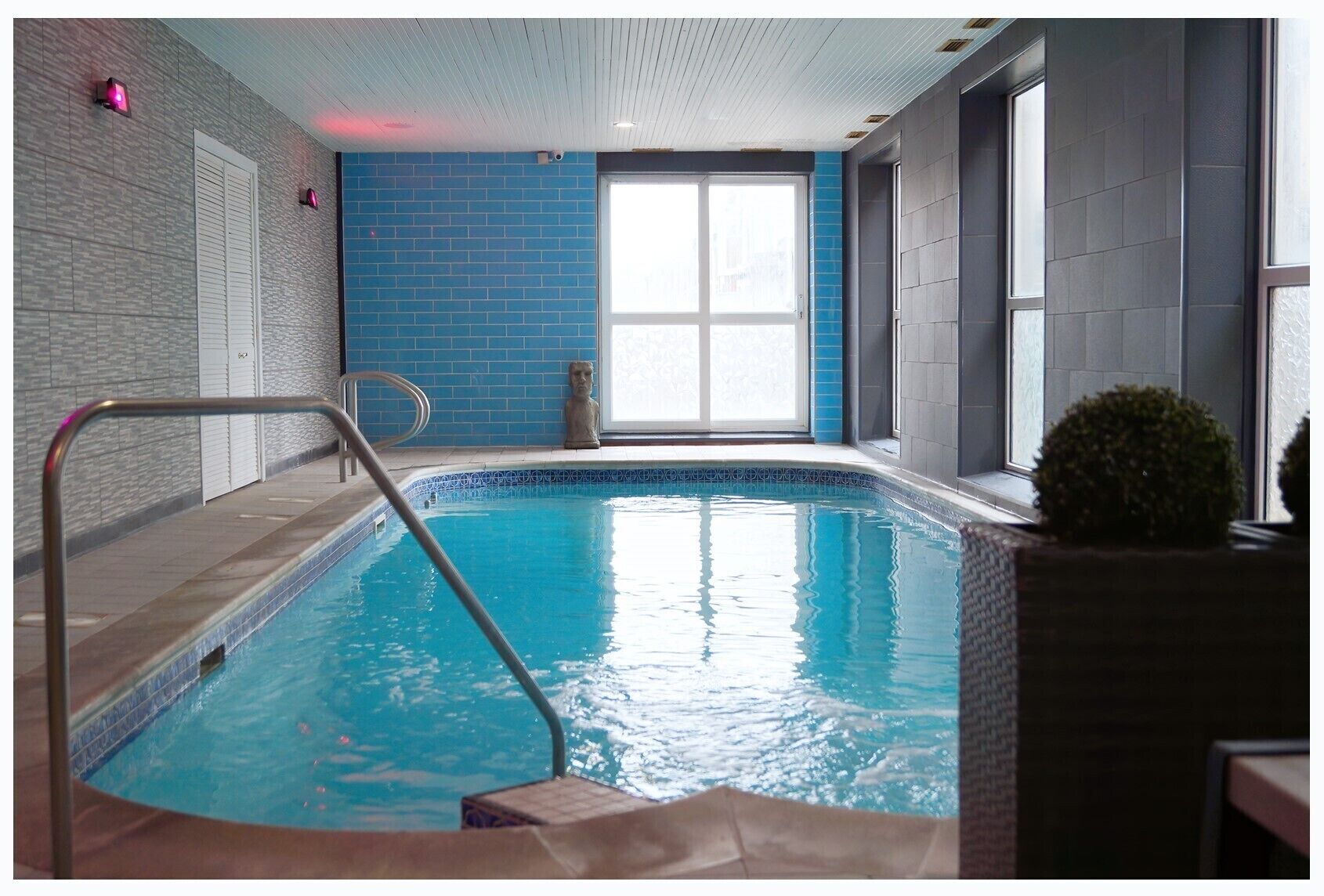 Una piscina interior con pared de azulejos azules, una ventana y una estatua.