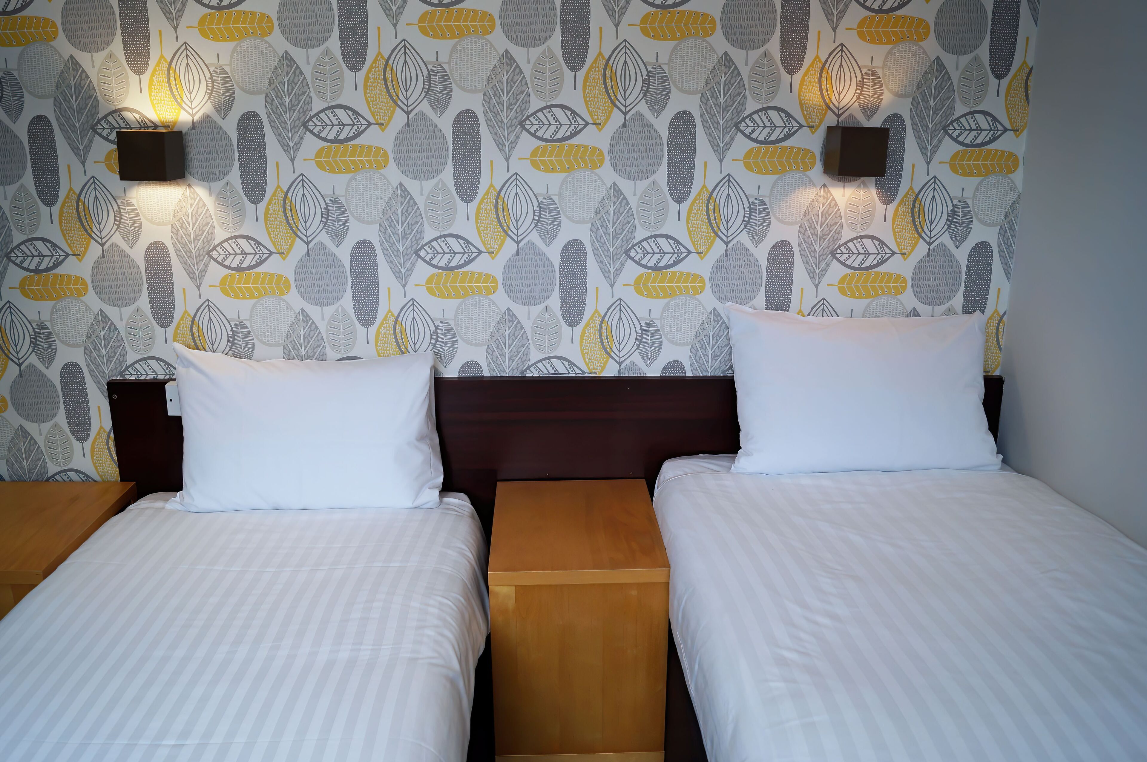 A hotel room with two beds, a wooden nightstand, and a patterned wallpaper with leaf designs.