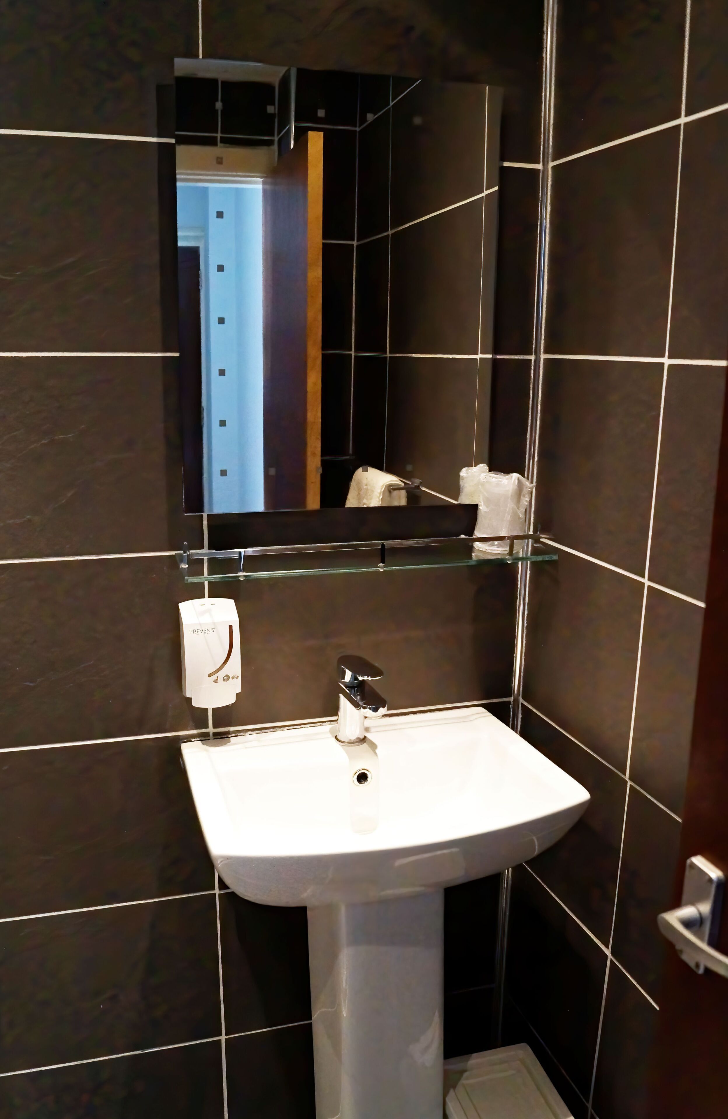 A modern bathroom with a white pedestal sink, a glass shelf above the sink, and a mirror above the sink.
