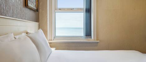 A hotel room with a large bed, a window with a view of the sea, and a framed picture on the wall.
